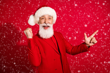Photo of cheerful winner adviser santa claus direct finger empty space wear x-mas hat suit on red color background
