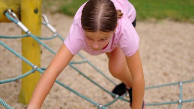 Preteen girl playing in a park. She is climbing through ropes.