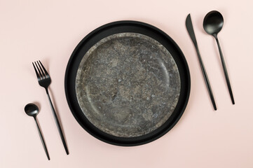 Top view of brown marble plate, black plate and cutlery on pink background. Food presentation,...