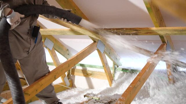 House attic insulation - construction worker installing cellulose on the roof