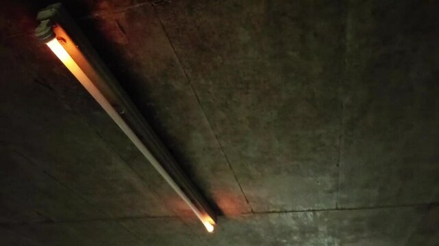 Flickering neon tube in garage with scary malfunction and dysfunction of neon lights flickers glowing and alarming or threatening in halloween atmosphere dramatic darkness gaslight with error switch
