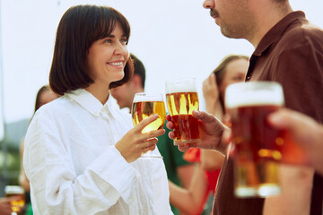 Group of friends clinking beer glasses, celebrating their meeting outdoor. Young people looks happy and cheerful. Concept of Friday mood, celebration, lunch break and Oktoberfest.