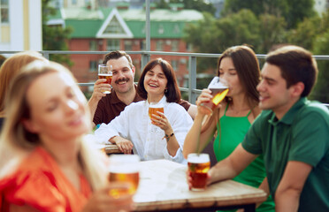 Group of friends sitting at pub terrace talking, drinking alcohol, celebrating meeting after long years. Festive atmosphere. Concept of Friday mood, celebration, lunch break and Oktoberfest.