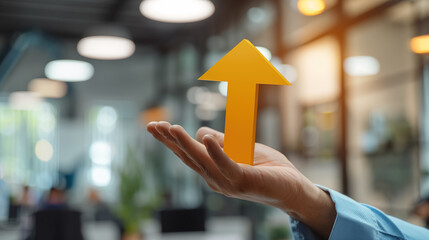close-up of a hand holding a yellow upward-pointing arrow, symbolizing growth, success, or a positive trend.