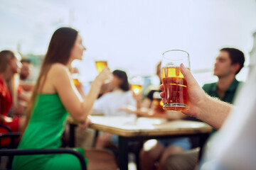 Unrecognizable man holding glass of beer. Sunlight reflects in golden liquid, enhancing moment. Concept of Friday mood, celebration, beverage, Oktoberfest, culture.