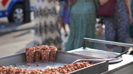 Close-up of caramelized nuts at a street food cart, with blurred people in the background..