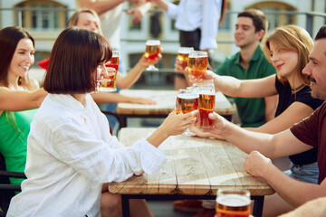 Friends gather around table, raising their glasses in toast to good times. Lively atmosphere and shared laughter make for perfect sunny day. Concept of Friday mood, celebration, Oktoberfest.