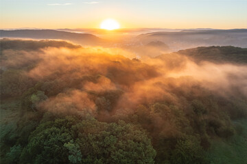 Aerial scene above the forest on Via Transilvanica. Foggy landscape above the green oak trees