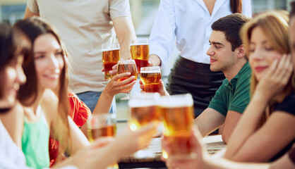 Joyful group enjoys cold beers on terrace, clinking glasses and smiling, celebrating friendship and simple pleasures of life. Concept of Friday mood, celebration, lunch break and Oktoberfest.