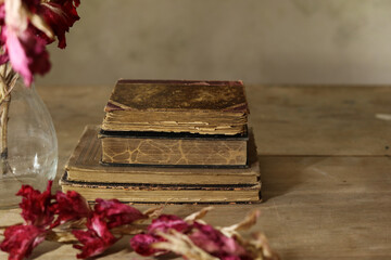 a still life with a pile of vintage books and dried red flowers	