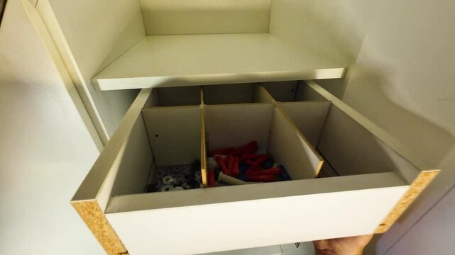Person putting in a handmade drawer full of nails and screws to the cabinet.