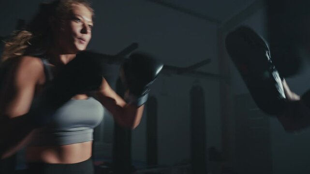 Intense boxing training session with a female athlete in a dark gym setting