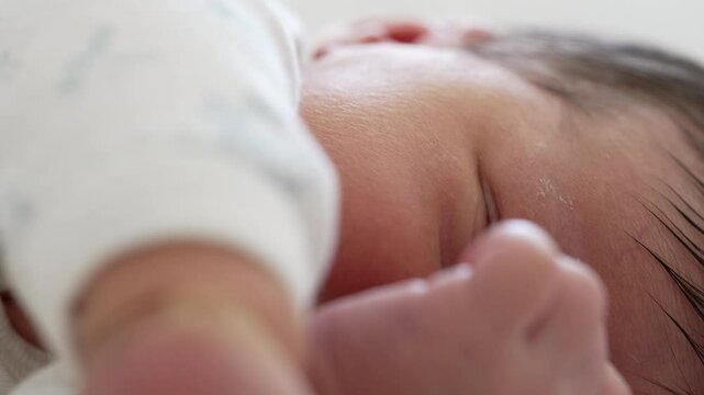 Close-up of a newborn baby gesticulating in sleep, with tiny hand movements and a slight grimace on the baby's face