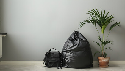 Black bean bag chair, houseplant and backpack near light grey wall in room. Space for text