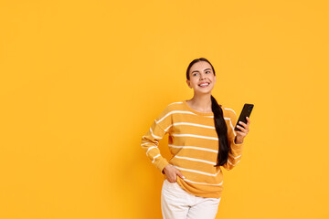 Smiling woman with smartphone on yellow background. Space for text