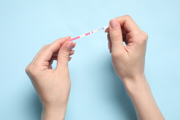 Woman holding pregnancy test on light blue background, top view