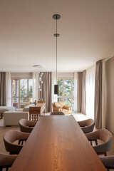 Large wooden table in a dining room. Around it beige-brown armchairs very comfortable. In the background is the living room.