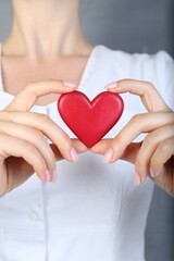 Doctor holding red heart on grey background, closeup