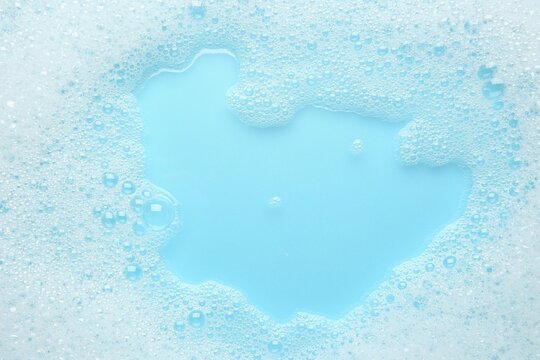 Washing laundry. White foam with bubbles on light blue background, top view