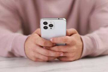 Man using smartphone at white table indoors, closeup