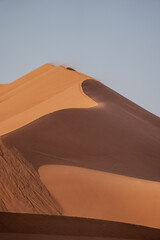 Wind blowing sand over the top of a giant sand dune at sunrise in Sossusvlei, Namibia