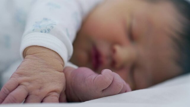 Newborn baby sleeping with hand and foot in focus, emphasizing the delicate and gentle nature of early infancy in a cozy setting