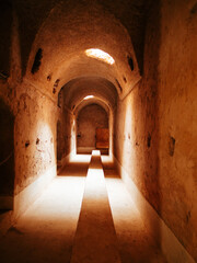 A tranquil and dimly lit ancient corridor showcasing intricate stonework and soft sunlight...