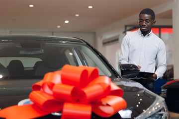 Young African salesman selling cars in showroom use tablet for insurance. Concept business sell car...