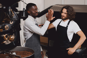 Happy friends african and caucasian mans workers in uniform working in coffee store roasting factory. Concept successfully implementing small business