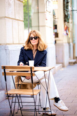 Attractive blond haired woman sitting at a table outside a cafe and using her smartphone