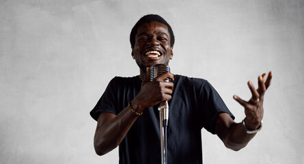 Young professional smiling energetic african man singer is performing song with retro microphone in...