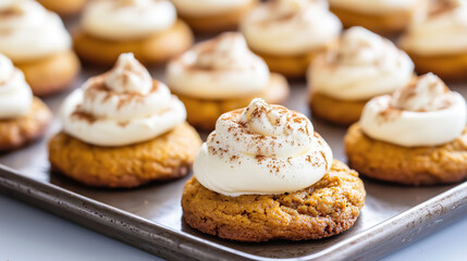 Freshly baked pumpkin cookies topped with creamy frosting, arranged on a baking tray.