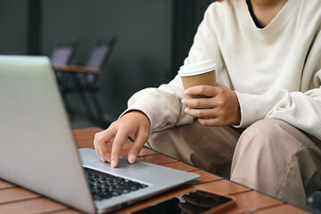 Woman typing on laptop computer while holding coffee cup