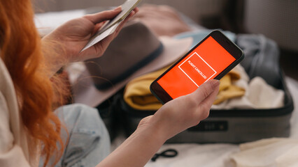 Unrecognizable traveler woman at bedroom holding mobile phone red screen sms message notification airline cancelled flight cancel problem female girl preparing trip travel trouble tickets passport