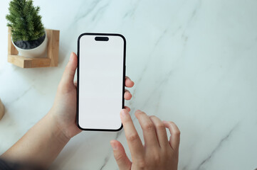 Close up shot of hands holding a smartphone with white empty screen over a marble table