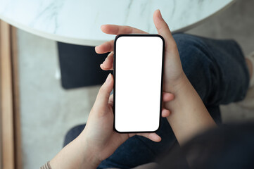 Woman holding a cell phone with a white screen sitting at a table. Modern technology and communication concept