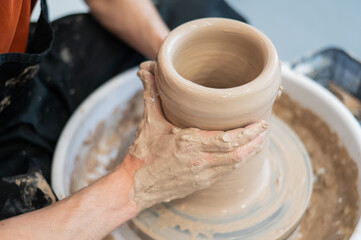 Close-up of a potter's hands making a ceramic vase on a potter's wheel. 