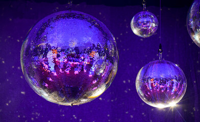 Disco balls hang from the ceiling in a colorfully illuminated hall and reflect the room in shades...