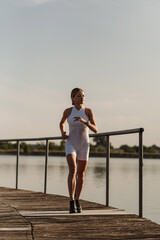 A woman in sportswear is jogging in the morning by the lake in the park