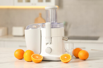 Modern juicer, oranges and glass on white marble table in kitchen