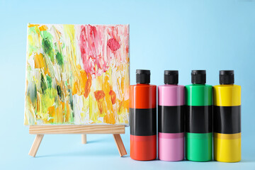 Acrylic paints of different colors and small easel with abstract picture on light blue background