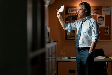 in the detective's office middle-aged investigator in a shirt and tie examines with a magnifying...