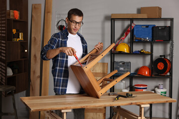 Man repairing wooden stool with screwdriver indoors