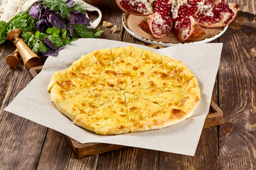 Traditional Ossetian Cheese Pie on Wooden Table with Herbs and Pomegranates