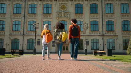 Back view three multiracial people outside go to class lesson studying together students diversity friends man guy male Caucasian African females women girls walking outdoor school university college