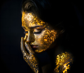 beautiful young woman with face covered golden paint; close-up of artistic feminine head; concept of beauty, nature, mask, luxury cosmetics, art, feminism; black background; copy space