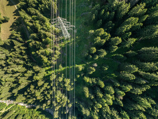 Aerial view of power line pylon in alpine forest in Switzerland. Electric current distribution with power grid.