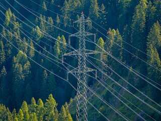 Aerial view of power line pylon in alpine forest in Switzerland. Electric current distribution with power grid.
