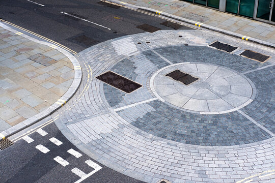 High-angle view of a roundabout with a cobblestone design, dual crosswalks, and adjacent structures representing a typical modern urban road complex.