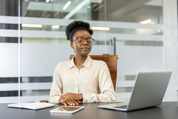 African American businesswoman meditating at desk in office. Woman practicing relaxation techniques...